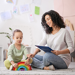 A female therapist works with a preschool child on the floor of a play room