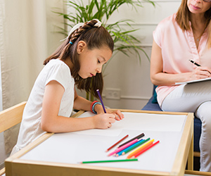 Elementary school girl takes an assessment as an evaluator looks on